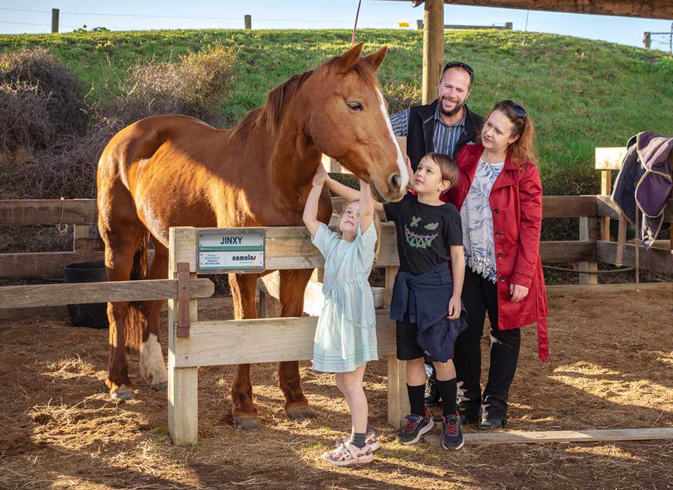 Ben and Karen Solomon with their two children pat the Riding for the Disabled pony they sponsor. The pony, named Jinky, is a chestnut with a white blaze from her forehead to nose.